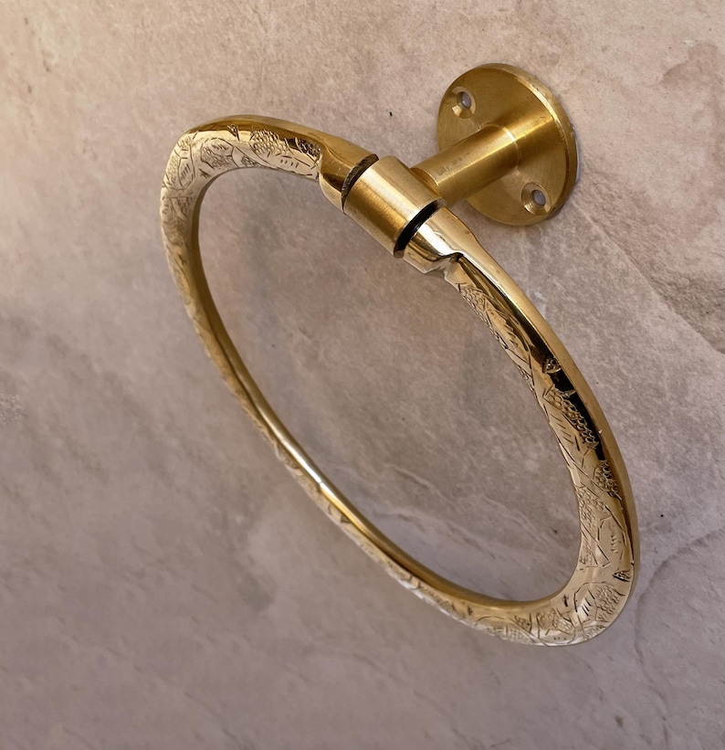 Pu&ograve; includere: Un portasciugamani dorato a forma ovale con motivo floreale. L'anello &egrave; montato su una base rotonda con fori per viti. Il metallo ha una finitura lucida e il disegno &egrave; inciso sulla superficie.