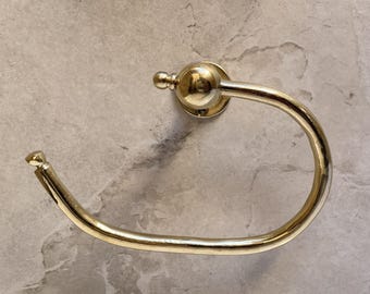 May include: A gold-colored, circular towel ring with a decorative ball finial. The ring is mounted on a circular base and is designed to hold a towel. The metal has a shiny finish.