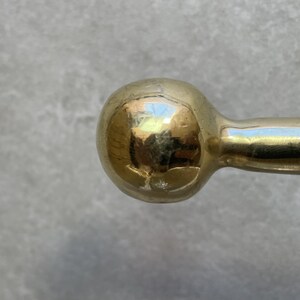 May include: Close-up of a gold-colored, spherical door handle. The handle has a smooth, reflective surface, with a rounded ball shape at the end. The handle appears to be made of metal and is likely for a door or cabinet.