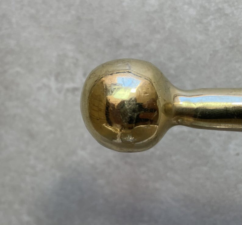 May include: Close-up of a gold-colored, spherical door handle. The handle has a smooth, reflective surface, with a rounded ball shape at the end. The handle appears to be made of metal and is likely for a door or cabinet.