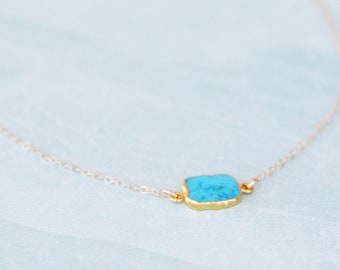 May include: A delicate gold chain necklace with a turquoise stone pendant. The stone is a light blue colour and has a slightly irregular shape.