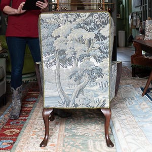 Peut inclure: Fauteuil rembourré avec une scène de paysage détaillée dans des tons de bleu et de gris. La chaise a des pieds en bois foncé et une bordure verte. L'arrière-plan comprend une femme tenant une tablette, une grande lanterne en papier et un tapis à motifs.