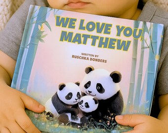 May include: A children's book titled "We Love You, Matthew" with a panda family illustration. The cover features a panda family in a bamboo forest setting. The book is held by a child.