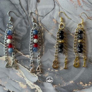 May include: Two pairs of dangle earrings. The first pair features silver-tone chains with blue, red, and white beads and the number 24 charms. The second pair features gold-tone chains with black and gold-tone beads and the number 8181 charms.