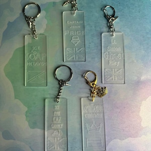 May include: Clear acrylic keyrings with silver fixings. Each keyring displays a name and a graphic, including the Union Jack flag, a crown, and a helmet. The keyrings are rectangular.