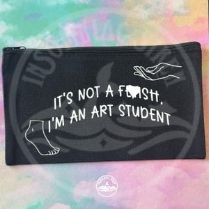 May include: Black canvas pencil case with a zip closure. The text "IT'S NOT A FLASH, I'M AN ART STUDENT" is printed in white. The design includes white illustrations of a tooth, a foot, and a hand.