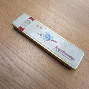 Può includere: Astuccio rettangolare con finiture dorate e parte superiore color argento chiaro. La parte superiore presenta il testo "Wolff's" e "Royal Sovereign BRITISH MADE PENCILS". Un emblema rosso e bianco è in alto a sinistra.