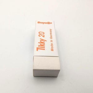 May include: A white rectangular eraser with a matching white box. The box features the orange text "Tikky 20" and "Made in Germany" with the Rotring logo. The eraser is a stationery item.