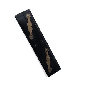May include: A rectangular black wooden object featuring two decorative brass-toned metal plates attached to the surface. Each metal plate has a curved, ornate shape and is secured with small circular rivets at the top and bottom ends.
