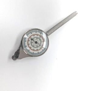 Op de afbeelding: Een zilverkleurige kaartmeter met een ronde wijzerplaat die verschillende schalen weergeeft, waaronder mijlen, kilometers en zeemijlen. Het instrument heeft een lange, getextureerde handgreep en een klein wieltje aan de basis voor metingen.