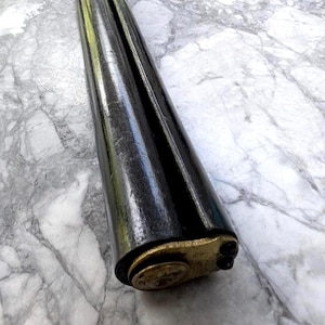 May include: A dark, glossy, double-barreled shotgun with a brass end cap. The barrels are black and reflect light. The shotgun is angled, showing the end with two small holes.