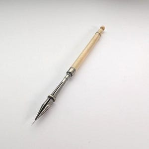 以下が含まれることがあります： 丸みを帯びた端を持つ長く細いクリーム色のハンドルと、銀色の金属製フェルールを備えたディップペン。ペン先は磨かれた銀色の金属製で、インクの流れを良くするためのスリットが入った尖った形状をしています。
