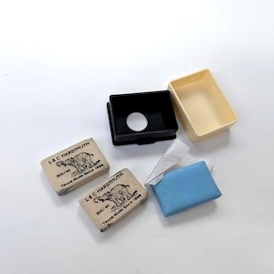 May include: Two rectangular tan cardboard boxes with black elephant illustrations and the text L & C HARDTMUTH 300/40 TRADE MARK SINCE 1896, a black plastic lid with a circular cutout, a cream-colored plastic tray, and a blue rectangular block.