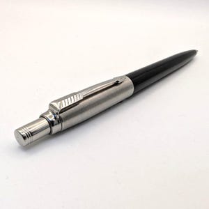 Op de afbeelding: Een slanke, zilveren en zwarte pen met een metallic afwerking. De pen heeft een zilveren clip en een zwarte schacht. De pen is ontworpen om mee te schrijven en is een klassiek schrijfinstrument.