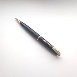 Puede incluir: Un elegante bolígrafo negro con detalles en tono dorado, que incluyen una punta afilada, una banda central y un clip con un diseño texturizado en forma de flecha en la parte superior. El bolígrafo tiene un acabado liso y brillante.