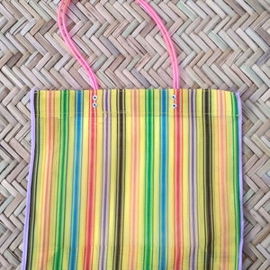 K&ouml;nnte beinhalten: Eine bunte, gestreifte Netztasche mit rosa Henkeln. Die Tasche besteht aus feinem Netzmaterial und hat einen gelben Hintergrund mit Streifen in Rot, Orange, Gelb, Gr&uuml;n, Blau, Lila und Schwarz.