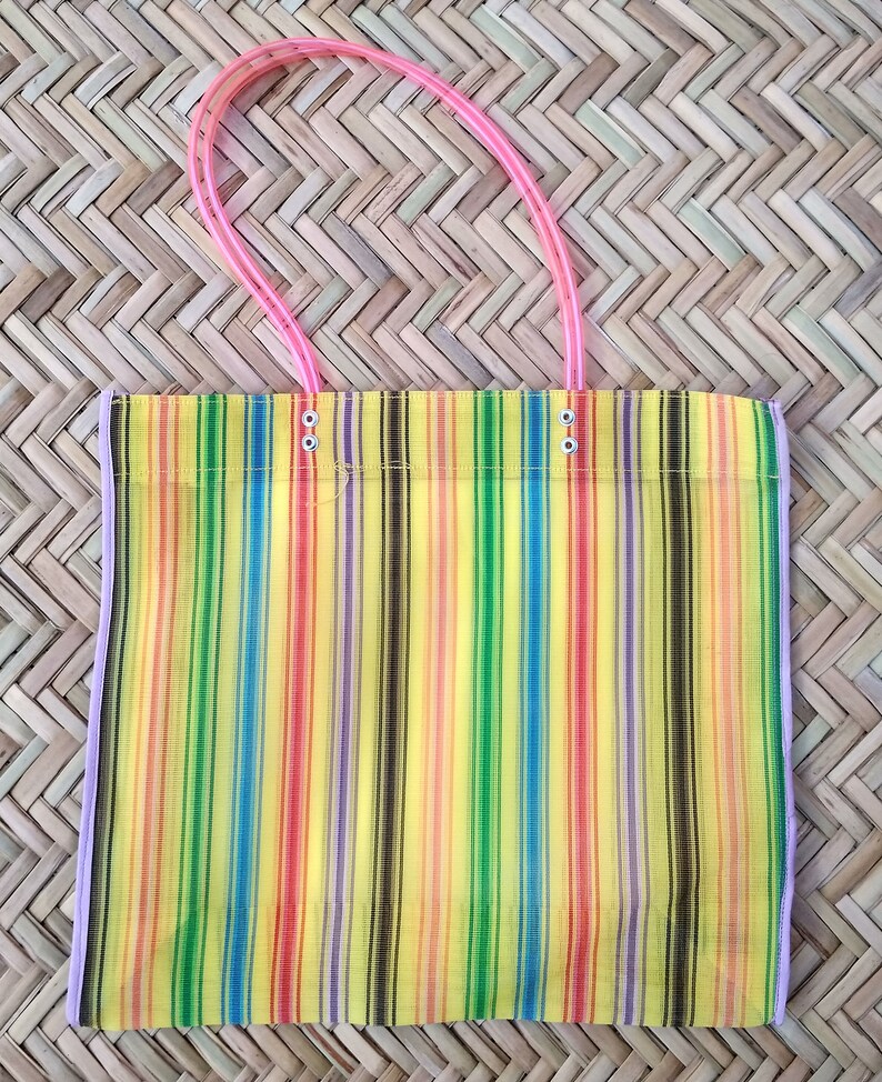 K&ouml;nnte beinhalten: Eine bunte, gestreifte Netztasche mit rosa Henkeln. Die Tasche besteht aus feinem Netzmaterial und hat einen gelben Hintergrund mit Streifen in Rot, Orange, Gelb, Gr&uuml;n, Blau, Lila und Schwarz.