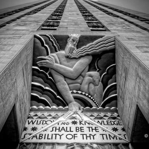Pode incluir: Fotografia a preto e branco de um edifício com uma escultura em relevo de uma figura segurando um cajado. A escultura é cercada por nuvens e o texto "Wisdom and Knowledge Shall Be The Stability Of Thy Times" está abaixo da escultura.