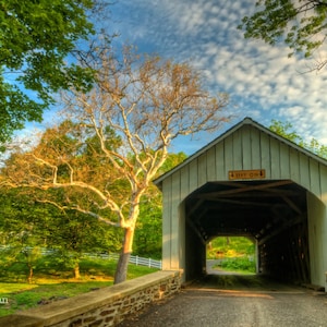 Puede incluir: Un puente cubierto de madera blanco con un letrero que dice "The Old Mill" en un entorno rural. El puente está rodeado de árboles verdes y un muro de piedra.
