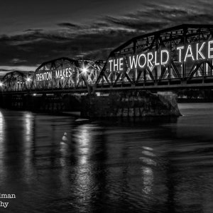 May include: A black and white photo of a bridge at night with the words "Trenton Makes The World Takes" illuminated on the bridge.
