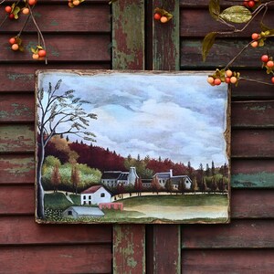 May include: A painting on wood depicting a small village with houses, trees, and a cloudy sky. The painting is framed with a rustic wooden frame.