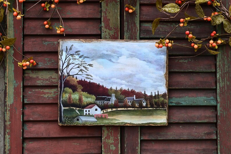 May include: A painting on wood depicting a small village with houses, trees, and a cloudy sky. The painting is framed with a rustic wooden frame.