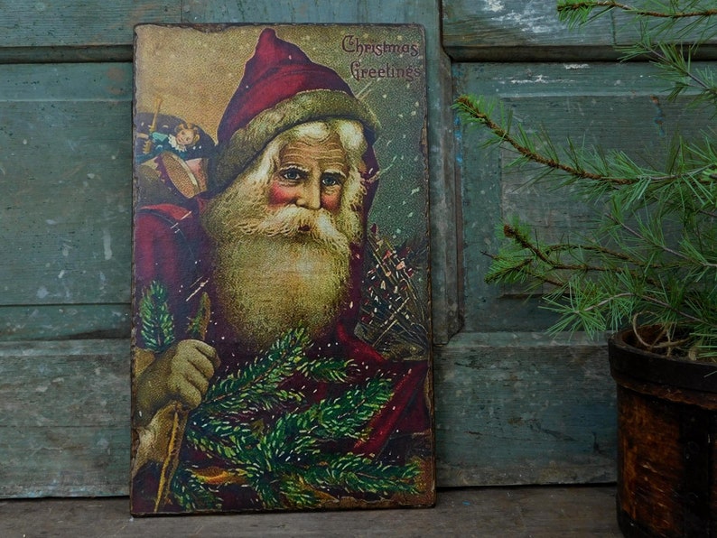 Peut inclure: Carte de No&euml;l vintage repr&eacute;sentant le P&egrave;re No&euml;l tenant une branche de sapin. La carte est dans les tons rouge, vert et or et comprend le texte "Christmas Greetings".