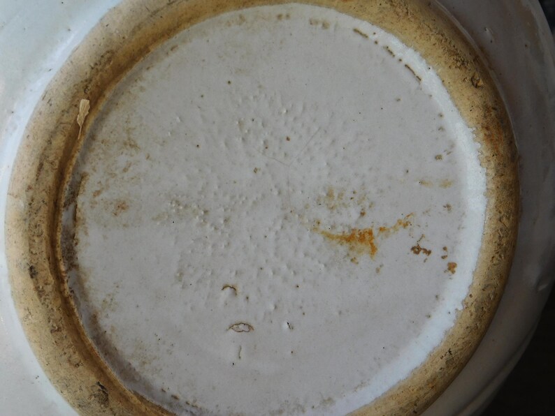 May include: Close-up of the bottom of a white ceramic bowl. The bowl's interior is a smooth, off-white color, while the rim and base have a textured, light brown appearance. The bowl shows signs of wear and age.