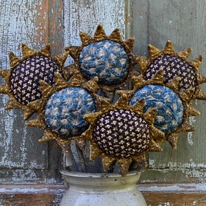 May include: A bouquet of six handmade fabric sunflowers in a rustic ceramic vase. The sunflowers are made with a blue and white floral print fabric and a brown and white floral print fabric. The sunflowers have gold-colored petals and are arranged in a vase with a distressed white finish.