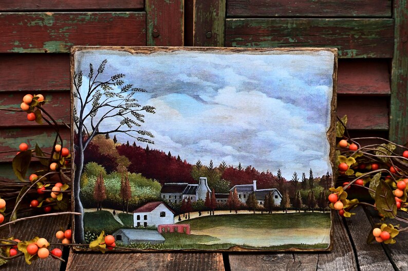 May include: A painting on wood depicting a small village with houses and trees under a cloudy sky. The painting is framed with a rustic wooden frame.