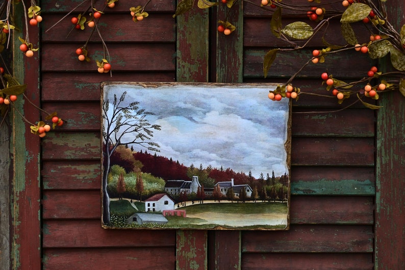 May include: A framed painting depicting a rural landscape with a small village nestled among trees. The sky is a soft blue with fluffy white clouds. The trees are a mix of green and brown, and the houses are white with red roofs. The painting is set against a rustic wooden background.