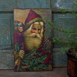 Peut inclure: Carte de No&euml;l vintage repr&eacute;sentant un P&egrave;re No&euml;l en costume rouge tenant une branche de pin. La carte a un fond enneig&eacute; et le texte "Christmas Greetings" en haut.