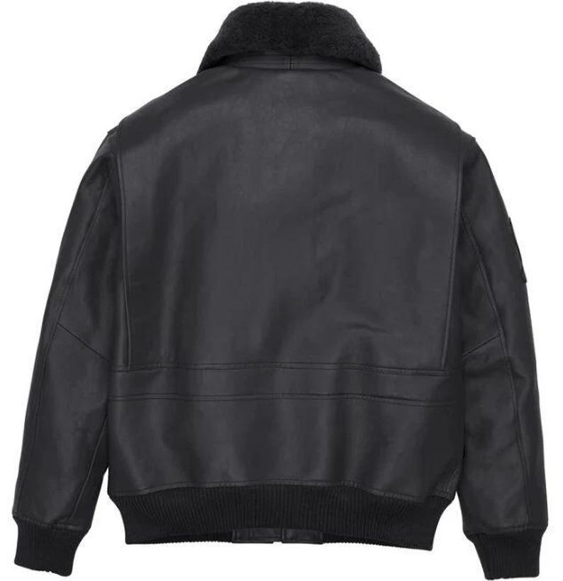 May include: A black leather bomber jacket featuring a dark gray faux fur collar, long sleeves with ribbed cuffs, and a ribbed hem. The back of the jacket displays a smooth leather finish with horizontal seam detailing across the mid-section.