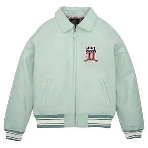 May include: A light mint green jacket with a full-length front zipper, a classic collar, and ribbed cuffs and hem featuring white stripes. The chest displays an embroidered patch with the text AVIREX and a shield graphic with a flag design.