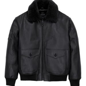 May include: A black leather bomber jacket featuring a black faux fur collar, a central zipper closure, and two front flap pockets with button fasteners. The jacket includes ribbed cuffs and hem, with a small patch detail on the right sleeve.