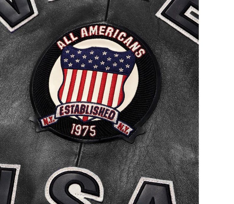 May include: A black leather jacket featuring a circular embroidered patch with the text ALL AMERICANS ESTABLISHED 1975 N.Y. and a shield graphic displaying the American flag. Large black letters with white trim are visible at the top and bottom edges.