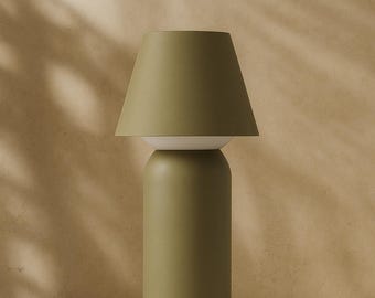 May include: A modern olive green table lamp with a cylindrical base and a conical lampshade. The lamp has a white section between the base and the shade. The background is a neutral beige.
