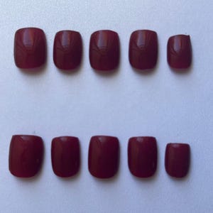 May include: A set of ten burgundy-colored, square-shaped artificial nails. The nails are arranged in two rows of five, showcasing a glossy finish. The color is a deep, rich shade of red.
