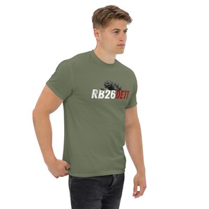 May include: An olive green t-shirt with the text "RB26DETT" in white and red, and a Godzilla graphic. The shirt is made of a soft material.
