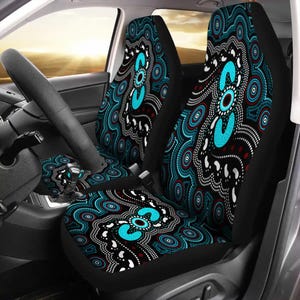 Puede incluir: Fundas de asiento de coche con un patrón circular turquesa, rojo y blanco sobre un fondo negro. El diseño se repite en la funda del volante. El interior del coche es visible, con el volante y el salpicadero.