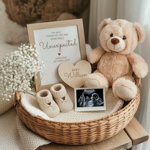 Puede incluir: Un anuncio de bebé con un marco que dice "Unexpected", un corazón de madera con el nombre "Willson", patucos, una ecografía y un osito de peluche, todo en una cesta de mimbre.