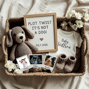 Puede incluir: Una cesta de mimbre contiene un juguete de perro tejido, un letrero enmarcado con "PLOT TWIST IT'S NOT A DOG!" y "JULY 2026", un body blanco con "Baby Willson", imágenes de ultrasonido y botines de bebé tejidos. Flores blancas adornan la escena.