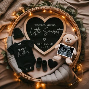 May include: A baby announcement with a black onesie that says "Baby Walker", a teddy bear holding an ultrasound image, and a heart-shaped sign that reads "We've been keeping Little Secret September 2025". The items are arranged in a woven basket.