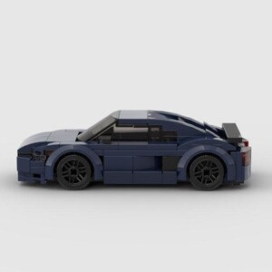 以下が含まれることがあります： ダークブルーのブロックでできたおもちゃの車。黒いホイール、スポイラー、流線型のデザインが特徴です。おもちゃの車はスポーツカーのミニチュアレプリカです。