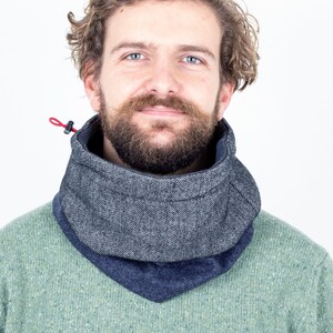 Może przedstawiać: Szary i granatowy ocieplacz na szyję z czerwoną sznurkiem. Ocieplacz na szyję jest wykonany z teksturowanej tkaniny i jest noszony wokół szyi. Osoba na zdjęciu ma na sobie zielony sweter.