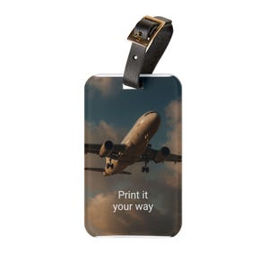 May include: Luggage tag featuring an image of an aeroplane in flight against a cloudy sky. The tag has a black leather strap with a gold-coloured buckle. The text "Print it your way" is printed on the tag.