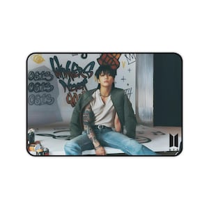 Könnte beinhalten: Rechteckiges Mauspad mit einer Person in einer grünen Jacke, einem weißen Hemd und einer blauen Jeans. Der Hintergrund zeigt Graffiti mit den Worten "Winners Never Quit" und den Zahlen "0613". Das BTS-Logo befindet sich in der unteren rechten Ecke.