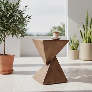 Puede incluir: Una mesa auxiliar geométrica de madera con un diseño único de reloj de arena. La mesa es de madera marrón claro y tiene una taza y un platillo pequeños encima. La mesa está rodeada de plantas en macetas y está sobre una superficie embaldosada.
