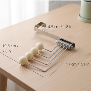 May include: A silver-colored over-the-door hanger with four cream-colored ball-tipped hooks. The hanger is 7.1 inches wide, 7.8 inches long, and the top hook is 1.8 inches long. The product is designed for hanging items.