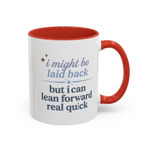 May include: White ceramic mug with a red interior and handle. The mug features the text "i might be laid back but i can lean forward real quick" in blue and gray lettering. The mug has a glossy finish.